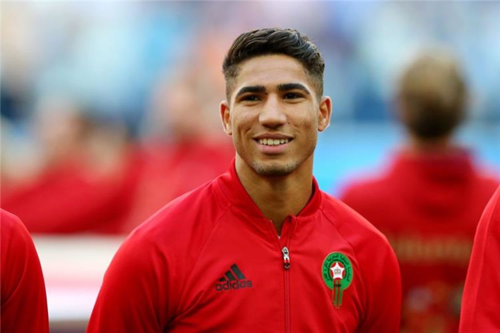  Achraf Hakimi, a Moroccan professional soccer player who plays for Paris Saint-Germain, wearing a red uniform smiles in front of the camera.